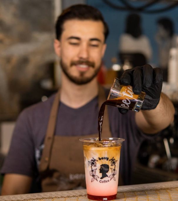 A smiling barista pouring espresso over an iced latte