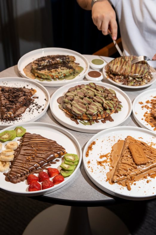 A table full of crepes and pancakes drizzled with chocolate, pistachio and Lotus